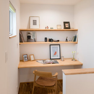 Modern home office and library in Nagoya with white walls, painted wood flooring, a built-in desk and brown floors.