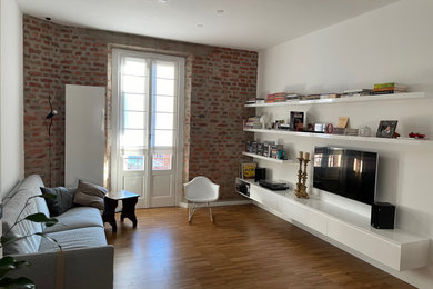 Immagine di un soggiorno minimalista di medie dimensioni e chiuso con libreria, pareti bianche, parquet chiaro, TV a parete e pavimento marrone