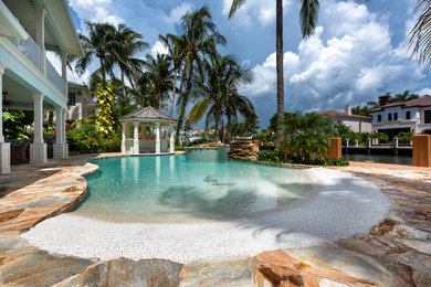 Design ideas for a mid-sized beach style backyard custom-shaped natural pool in Miami with a hot tub and natural stone pavers.