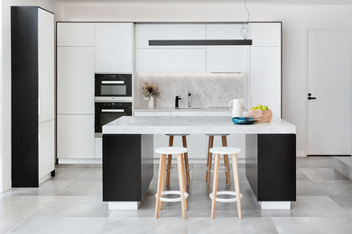 Photo of a mid-sized modern l-shaped open plan kitchen in Melbourne with a drop-in sink, white cabinets, limestone benchtops, grey splashback, stone slab splashback, black appliances, marble floors, with island and grey floor.