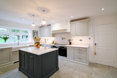 Inspiration for a large traditional grey and cream enclosed kitchen in Essex with a belfast sink, shaker cabinets, quartz worktops, white splashback, black appliances, an island, beige floors and white worktops.