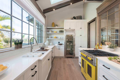 Example of a transitional l-shaped medium tone wood floor and brown floor kitchen design in Tampa with an undermount sink, recessed-panel cabinets, white cabinets, white backsplash, subway tile backsplash, colored appliances, no island and white countertops