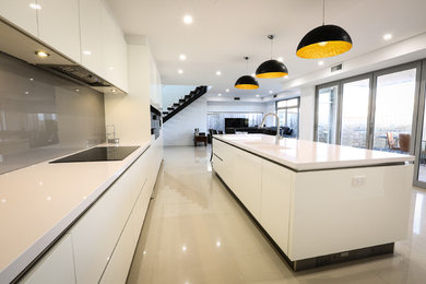 Photo of a mid-sized modern single-wall open plan kitchen in Sydney with an integrated sink, flat-panel cabinets, white cabinets, quartz benchtops, grey splashback, glass sheet splashback, panelled appliances, with island, beige floor and porcelain floors.