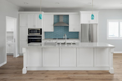 Example of a vinyl floor eat-in kitchen design in Los Angeles with an undermount sink, shaker cabinets, white cabinets, quartz countertops, blue backsplash, cement tile backsplash, stainless steel appliances, gray countertops and an island