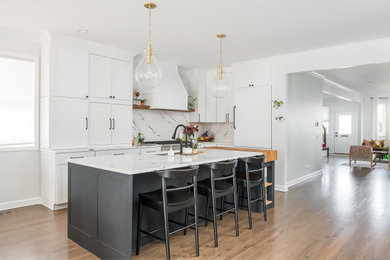 Example of a mid-sized transitional l-shaped medium tone wood floor and brown floor kitchen design in Chicago with an undermount sink, shaker cabinets, white cabinets, quartz countertops, white backsplash, quartz backsplash, paneled appliances, an island and white countertops