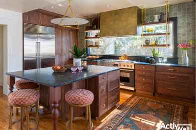 Open concept kitchen - mid-sized eclectic u-shaped medium tone wood floor and brown floor open concept kitchen idea in Other with recessed-panel cabinets, brown cabinets, green backsplash, ceramic backsplash, stainless steel appliances, an island and black countertops