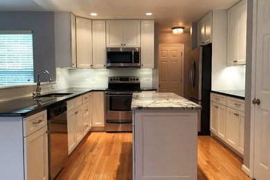 Inspiration for a large transitional l-shaped eat-in kitchen in Baltimore with an undermount sink, shaker cabinets, white cabinets, granite benchtops, white splashback, porcelain splashback, stainless steel appliances, light hardwood floors, with island, beige floor and black benchtop.