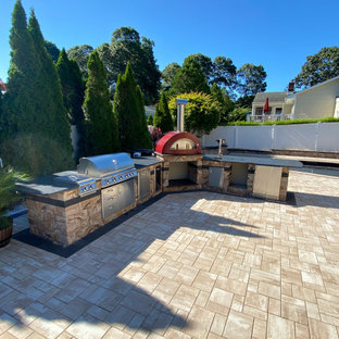 Diseño de cocina en L, moderna, grande, con fregadero bajoencimera, puertas de armario en acero inoxidable, encimera de granito, electrodomésticos de acero inoxidable, suelo de ladrillo, suelo beige y encimeras grises