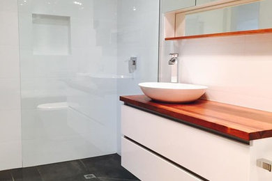 Photo of a mid-sized contemporary master bathroom in Melbourne with white cabinets, a corner tub, an open shower, a one-piece toilet, gray tile, porcelain tile, white walls, cement tiles, a vessel sink and wood benchtops.