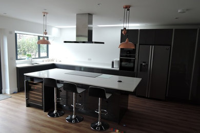 Design ideas for a modern l-shaped open plan kitchen in Surrey with flat-panel cabinets, black cabinets, an island and white worktops.