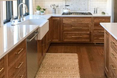 Mid-sized transitional u-shaped medium tone wood floor eat-in kitchen photo in Minneapolis with a farmhouse sink, shaker cabinets, medium tone wood cabinets, white backsplash, subway tile backsplash, stainless steel appliances, an island and white countertops