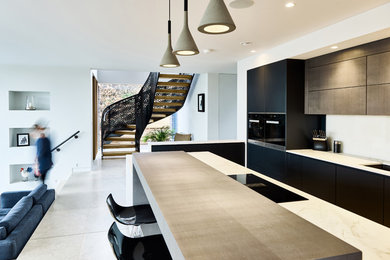 Photo of a contemporary open plan kitchen in Devon with an undermount sink, flat-panel cabinets, black cabinets, white splashback, black appliances, with island, grey floor and white benchtop.