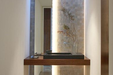 Example of a trendy beige tile and stone tile concrete floor powder room design in Los Angeles with white walls, a vessel sink, wood countertops and brown countertops
