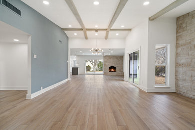 Example of a mid-sized minimalist open concept vinyl floor, brown floor and exposed beam living room design in Dallas with white walls, a standard fireplace, a stone fireplace and a wall-mounted tv