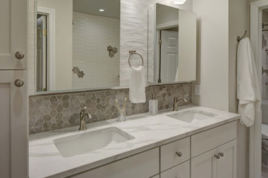Photo of a mid-sized transitional master bathroom in New York with recessed-panel cabinets, white cabinets, an alcove tub, an alcove shower, a bidet, multi-coloured tile, ceramic tile, beige walls, porcelain floors, an undermount sink, engineered quartz benchtops, beige floor, a sliding shower screen and white benchtops.