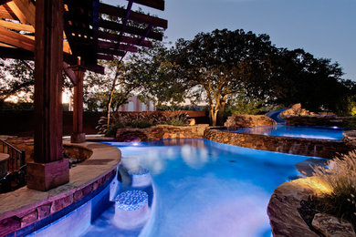 Design ideas for an expansive tropical backyard custom-shaped natural pool in Dallas with a water slide and natural stone pavers.