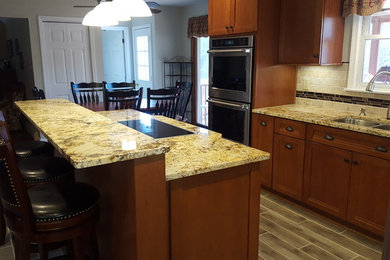 Example of a mid-sized classic l-shaped porcelain tile eat-in kitchen design in Philadelphia with a double-bowl sink, beaded inset cabinets, medium tone wood cabinets, granite countertops, beige backsplash, stone tile backsplash, stainless steel appliances and an island