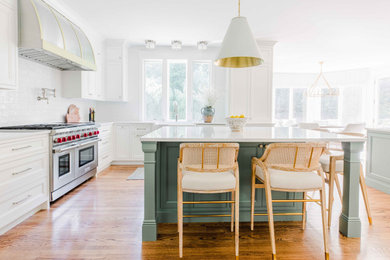 Large u-shaped medium tone wood floor and brown floor eat-in kitchen photo in Boston with a farmhouse sink, recessed-panel cabinets, white cabinets, quartz countertops, white backsplash, ceramic backsplash, stainless steel appliances, two islands and brown countertops
