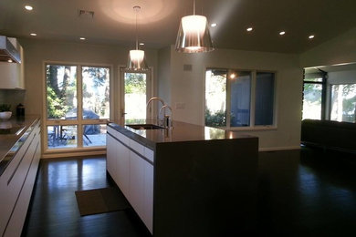 Example of a mid-sized transitional single-wall medium tone wood floor open concept kitchen design in Boston with a drop-in sink, flat-panel cabinets, white cabinets, granite countertops, white backsplash, stone tile backsplash, stainless steel appliances and an island