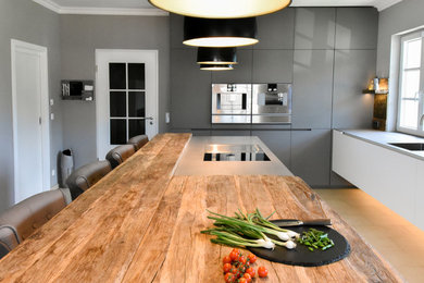 Offene, Zweizeilige, Große Industrial Küche mit integriertem Waschbecken, flächenbündigen Schrankfronten, weißen Schränken, Arbeitsplatte aus Holz, Rückwand aus Metallfliesen, Küchengeräten aus Edelstahl, Kücheninsel, Terrakottaboden und beigem Boden in Köln