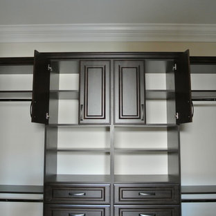 This is an example of a large traditional gender neutral walk-in wardrobe in Miami with raised-panel cabinets, dark wood cabinets and travertine flooring.