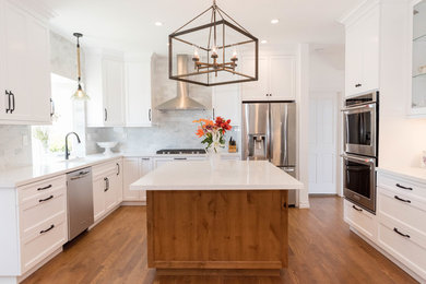 Expansive beach style u-shaped eat-in kitchen in San Francisco with a drop-in sink, white cabinets, quartz benchtops, grey splashback, ceramic splashback, stainless steel appliances, light hardwood floors, with island, brown floor, flat-panel cabinets and white benchtop.