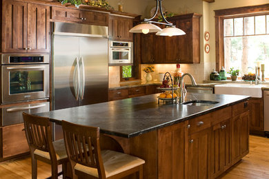 Inspiration for a large craftsman u-shaped medium tone wood floor open concept kitchen remodel in Phoenix with a farmhouse sink, shaker cabinets, medium tone wood cabinets, soapstone countertops, ceramic backsplash, stainless steel appliances, an island and beige backsplash