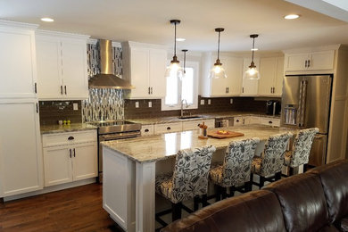 Example of a large transitional galley medium tone wood floor and brown floor open concept kitchen design in Other with an undermount sink, raised-panel cabinets, white cabinets, granite countertops, brown backsplash, ceramic backsplash, stainless steel appliances and an island
