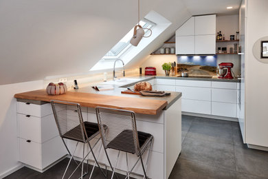 Mittelgroße Moderne Wohnküche ohne Insel in U-Form mit Unterbauwaschbecken, flächenbündigen Schrankfronten, weißen Schränken, Arbeitsplatte aus Fliesen, Küchenrückwand in Weiß, Glasrückwand, schwarzen Elektrogeräten, Keramikboden, grünem Boden und grauer Arbeitsplatte in Dortmund