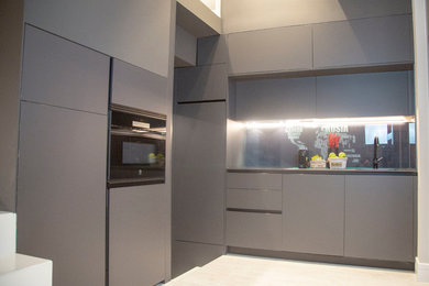 This is an example of a small modern l-shaped open plan kitchen in Madrid with black cabinets, black splashback, ceramic floors, no island and black benchtop.