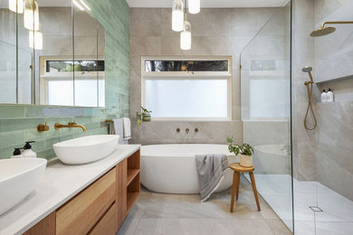 Photo of a large transitional master wet room bathroom in Melbourne with flat-panel cabinets, medium wood cabinets, a freestanding tub, a one-piece toilet, green tile, ceramic tile, grey walls, porcelain floors, a vessel sink, terrazzo benchtops, grey floor, an open shower, grey benchtops, a niche, a double vanity and a floating vanity.