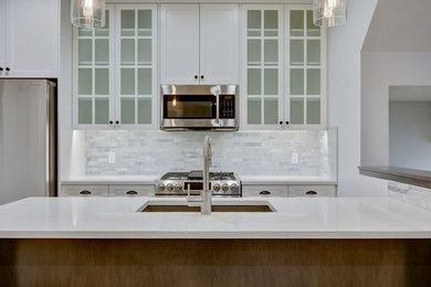 Trendy u-shaped light wood floor eat-in kitchen photo in Calgary with an undermount sink, shaker cabinets, white cabinets, quartzite countertops, white backsplash, stone tile backsplash, stainless steel appliances and an island