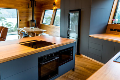 Contemporary open plan kitchen in Hobart with wood benchtops, black appliances, with island and grey benchtop.