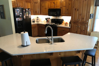 Inspiration for a mid-sized timeless l-shaped light wood floor and brown floor open concept kitchen remodel in Richmond with a double-bowl sink, raised-panel cabinets, medium tone wood cabinets, quartz countertops, black appliances, an island and gray countertops