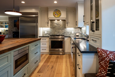 Example of a mid-sized transitional l-shaped light wood floor open concept kitchen design in Raleigh with a single-bowl sink, beaded inset cabinets, white cabinets, wood countertops, green backsplash, glass tile backsplash, stainless steel appliances, an island and black countertops