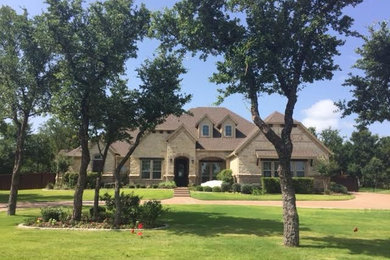 Large traditional beige two-story stone exterior home idea in Dallas with a clipped gable roof