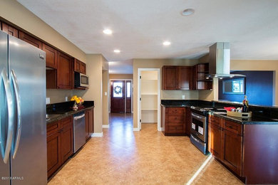 Mid-sized southwest l-shaped brown floor eat-in kitchen photo in Phoenix with recessed-panel cabinets, dark wood cabinets, granite countertops, stainless steel appliances, a peninsula and black countertops