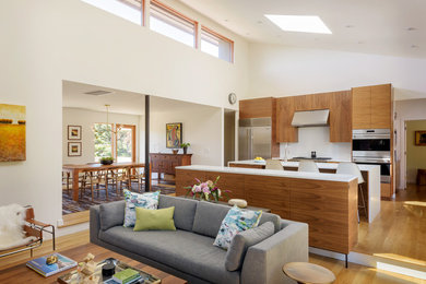 Photo of a mid-sized modern open plan kitchen in Portland with flat-panel cabinets, medium wood cabinets, stainless steel appliances, light hardwood floors, with island and white benchtop.