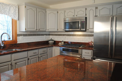 Inspiration for a mid-sized transitional l-shaped light wood floor open concept kitchen remodel in New York with a drop-in sink, raised-panel cabinets, black cabinets, granite countertops, gray backsplash, ceramic backsplash, stainless steel appliances and an island