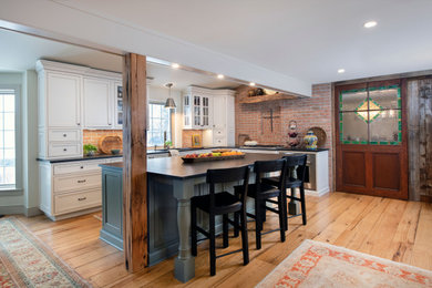 Large country l-shaped light wood floor kitchen photo in Philadelphia with a double-bowl sink, flat-panel cabinets, white cabinets, granite countertops, red backsplash, brick backsplash, stainless steel appliances, an island and black countertops
