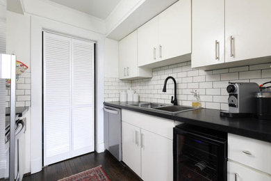 Kitchen pantry - mid-sized transitional galley dark wood floor and brown floor kitchen pantry idea in Birmingham with a drop-in sink, flat-panel cabinets, white cabinets, granite countertops, white backsplash, subway tile backsplash, stainless steel appliances, no island and black countertops