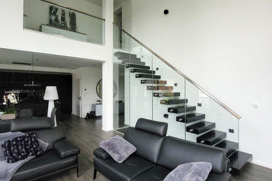 Cette image montre un grand escalier droit minimaliste avec un garde-corps en verre.