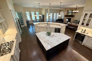 Example of a large transitional medium tone wood floor and brown floor kitchen design in Houston with an undermount sink, raised-panel cabinets, beige cabinets, quartzite countertops, beige backsplash, stone slab backsplash, stainless steel appliances, two islands and beige countertops