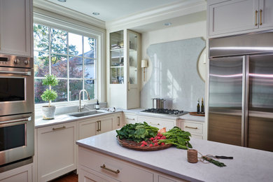 Bild på ett mellanstort vintage vit vitt kök, med en undermonterad diskho, skåp i shakerstil, vita skåp, bänkskiva i kvarts, vitt stänkskydd, rostfria vitvaror, mellanmörkt trägolv, en köksö och brunt golv
