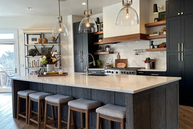 Inspiration for a mid-sized eclectic medium tone wood floor open concept kitchen remodel in Denver with a farmhouse sink, shaker cabinets, black cabinets, solid surface countertops, white backsplash, stainless steel appliances, an island and white countertops