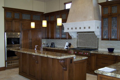 This is an example of a large country l-shaped eat-in kitchen in Other with an undermount sink, raised-panel cabinets, dark wood cabinets, granite benchtops, beige splashback, stone tile splashback, stainless steel appliances, terra-cotta floors and with island.