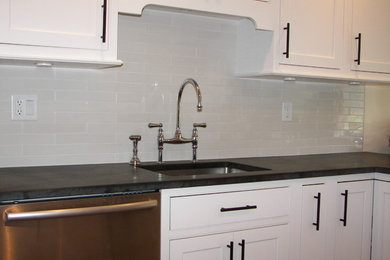 Example of a mid-sized classic galley ceramic tile enclosed kitchen design in New York with an undermount sink, shaker cabinets, white cabinets, soapstone countertops, white backsplash, ceramic backsplash, stainless steel appliances and a peninsula