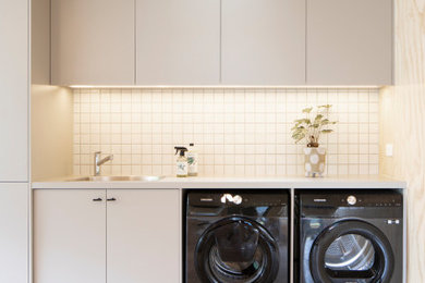 This is an example of a small contemporary single-wall utility room in Melbourne with a single-bowl sink, flat-panel cabinets, beige cabinets, laminate benchtops, white splashback, mosaic tile splashback, beige walls, concrete floors, a side-by-side washer and dryer, beige benchtop, wood and wood walls.