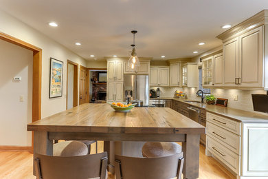 Inspiration for a timeless light wood floor kitchen remodel in Manchester with a double-bowl sink, raised-panel cabinets, beige cabinets, wood countertops, beige backsplash, ceramic backsplash, stainless steel appliances and an island