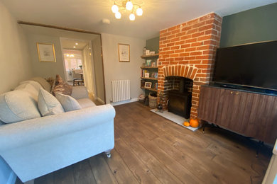 Design ideas for a medium sized rustic living room in Other with green walls, dark hardwood flooring, a wood burning stove, a brick fireplace surround, a corner tv, brown floors, brick walls and a chimney breast.